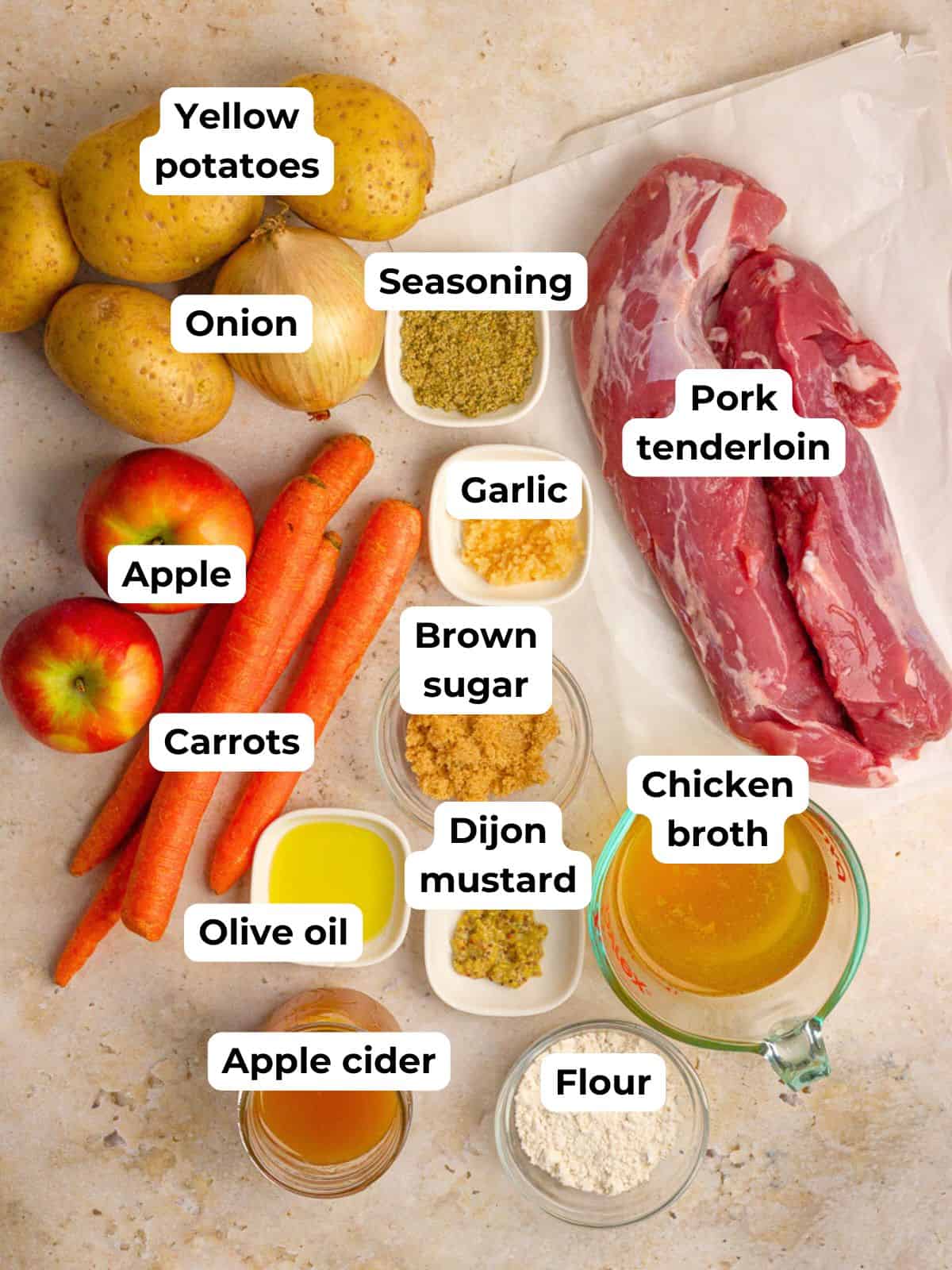 Ingredients for apple cider pork tenderloin including pork, apples, carrots, potatoes, and apple cider arranged on a counter.