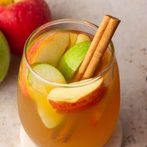 A fall drink scene featuring apple cider sangria with red and green apples and cinnamon sticks.