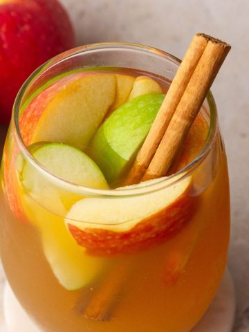 A fall drink scene featuring apple cider sangria with red and green apples and cinnamon sticks.