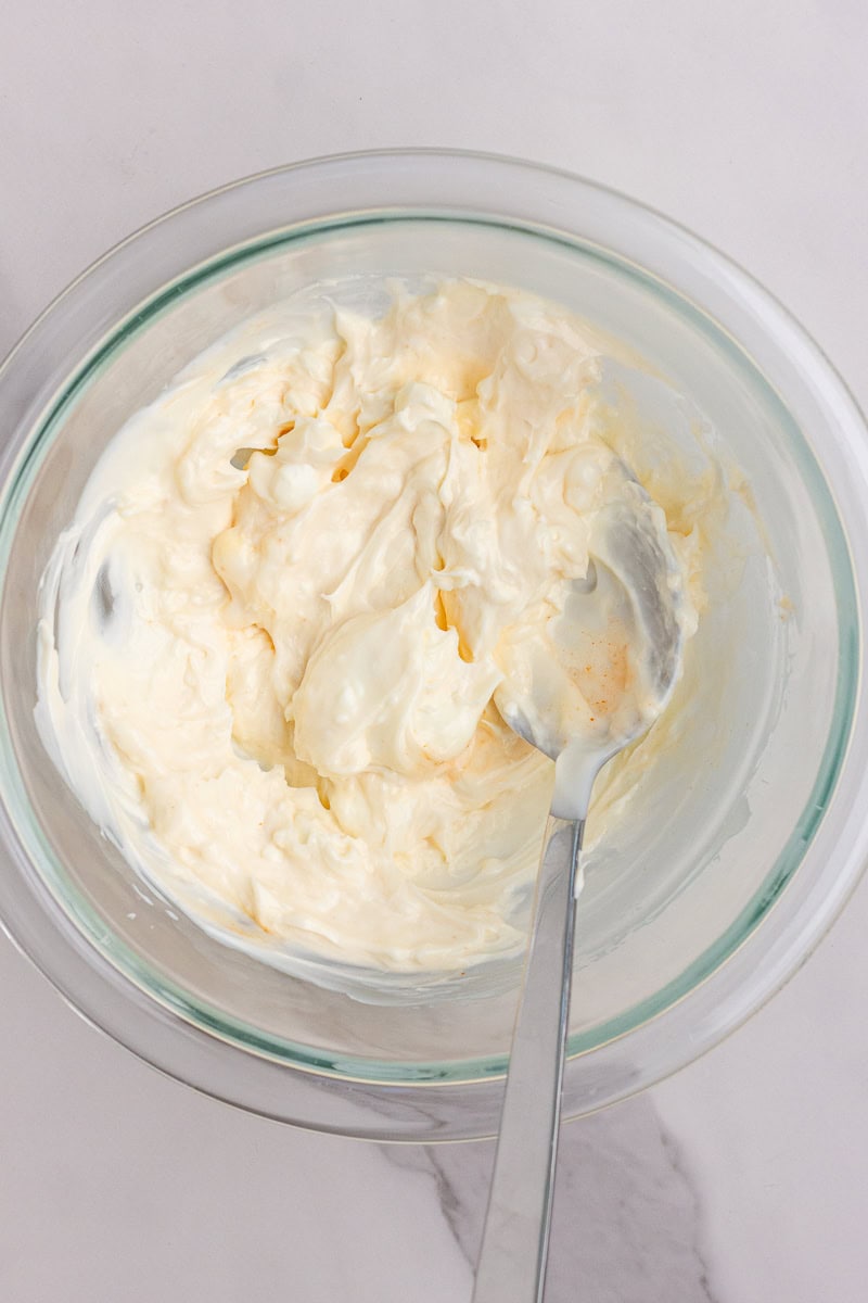 A glass bowl with cream cheese and mayonnaise mixture being stirred until smooth.