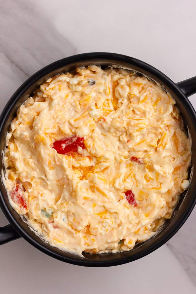 An unbaked pimento cheese mixture spread evenly in a small black baking dish before going into the oven.