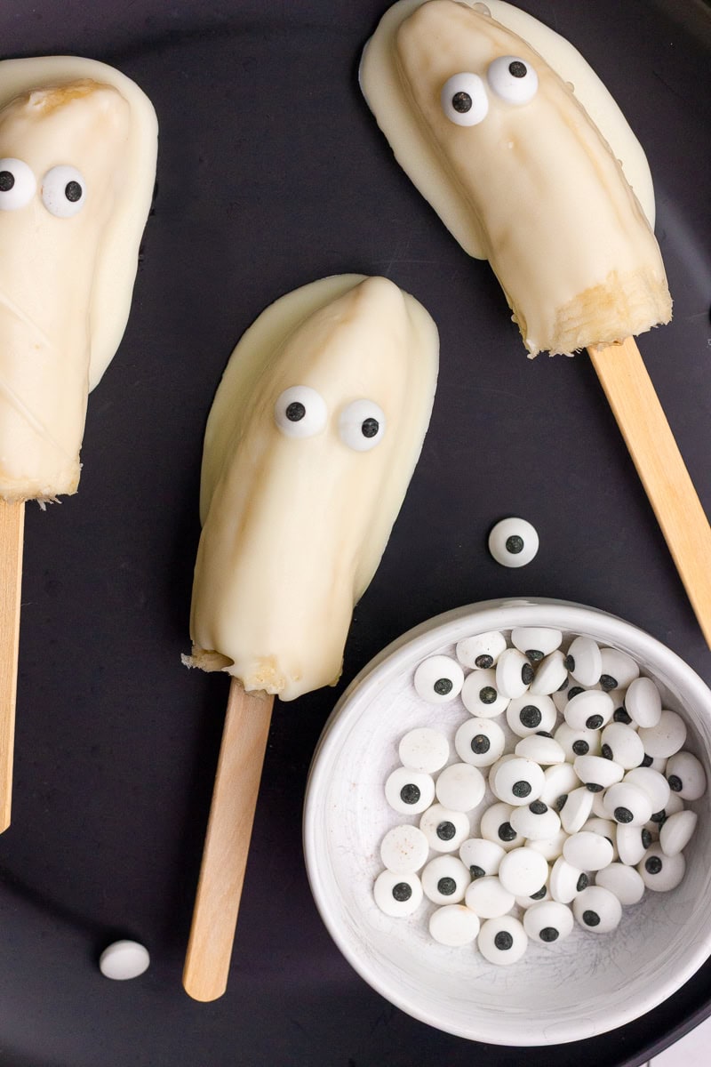 A black plate with three finished boonanas and a small bowl of candy eyes beside them.