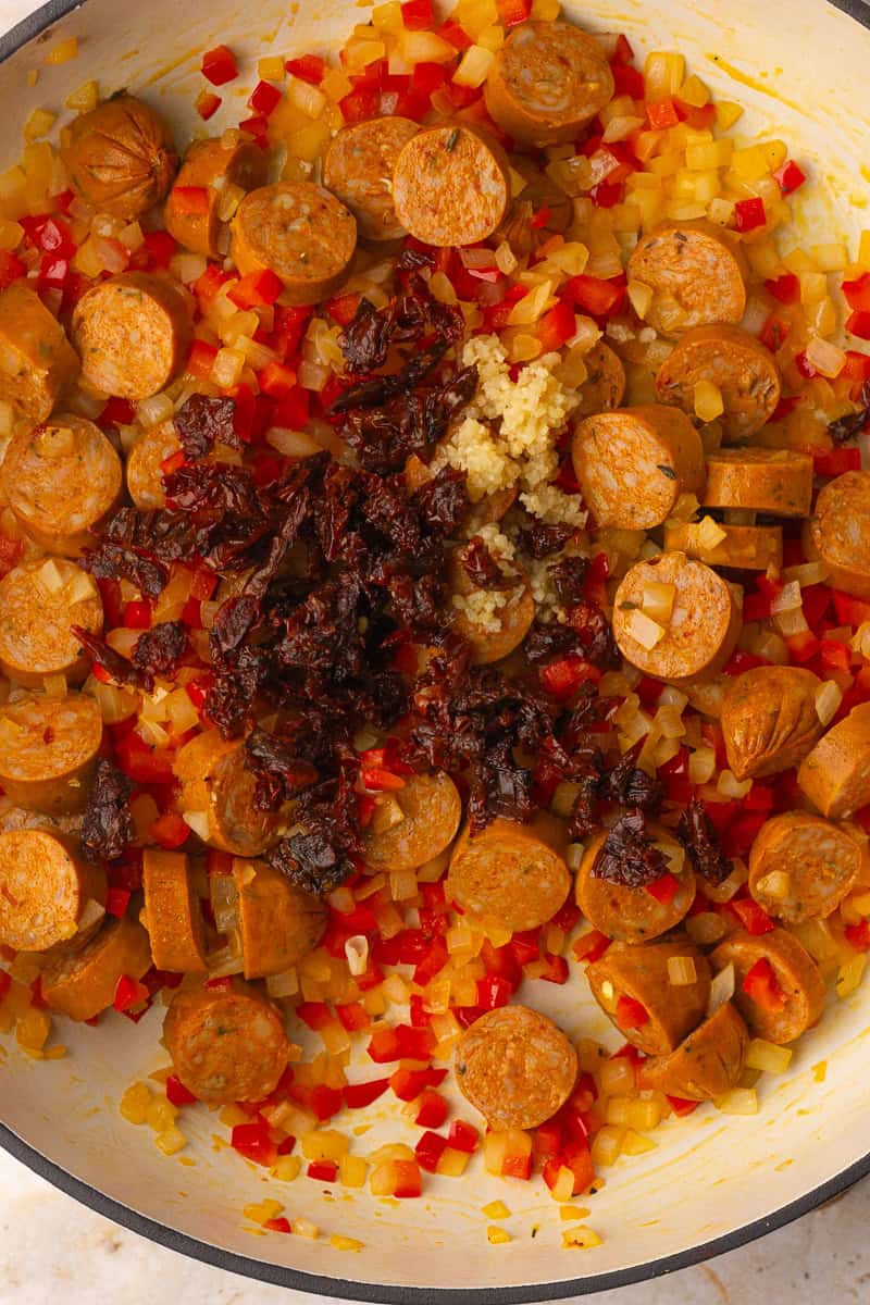 Browned andouille chicken sausage, minced garlic, and chopped sun-dried tomatoes are added to the softened peppers and onions in the skillet.