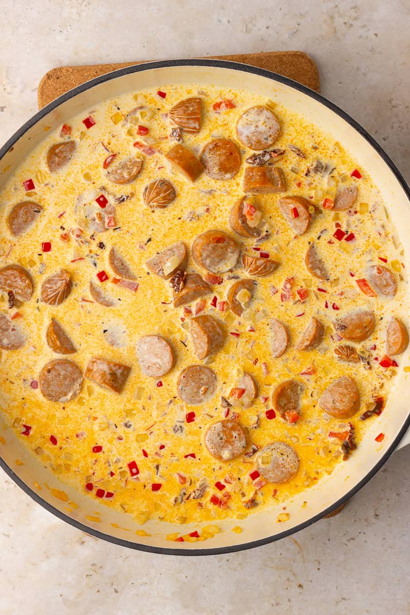 The skillet is filled with a creamy broth mixture simmering with sausage, onions, and red bell peppers.