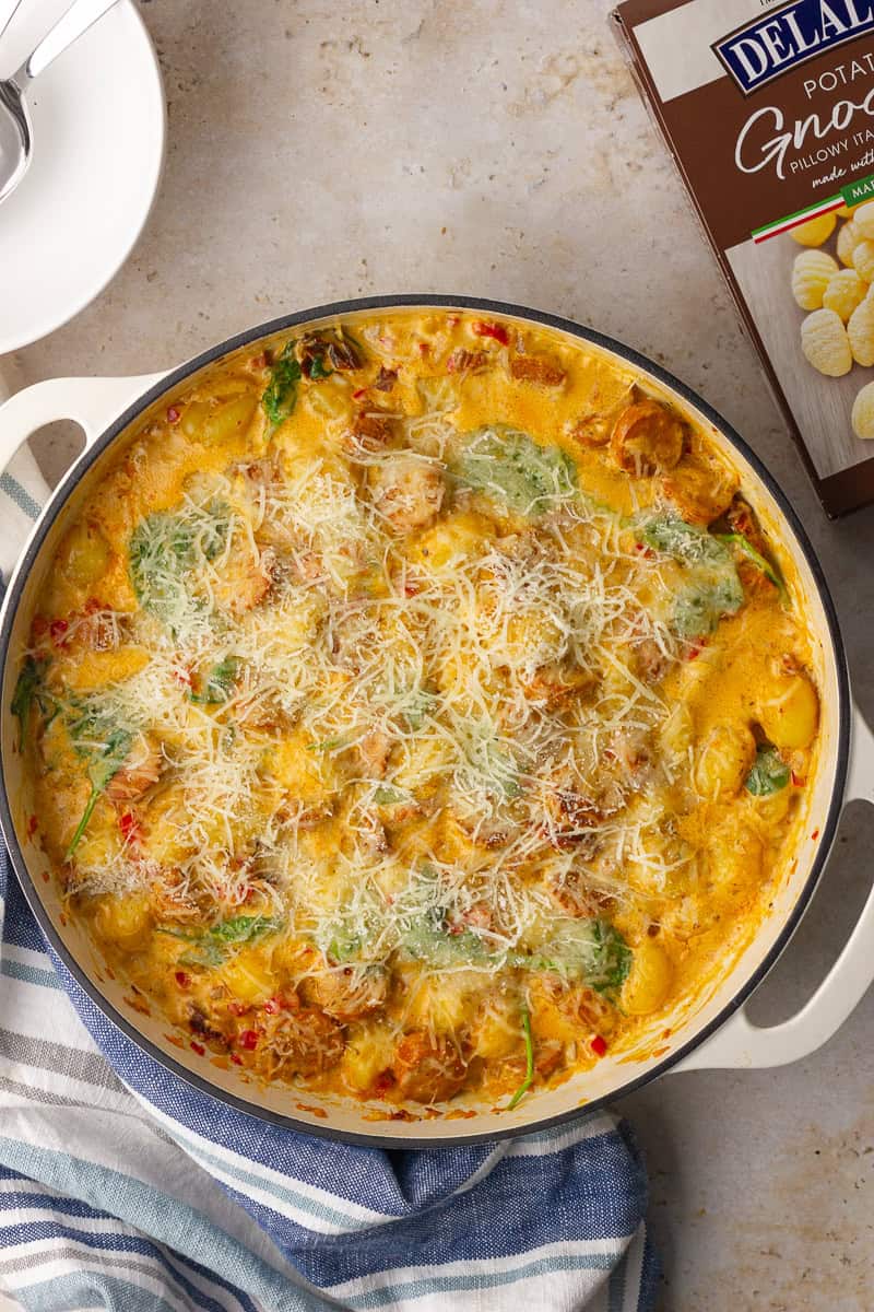 The baked Cajun gnocchi skillet is bubbly and topped with melted cheese with a box of gnocchi nearby.