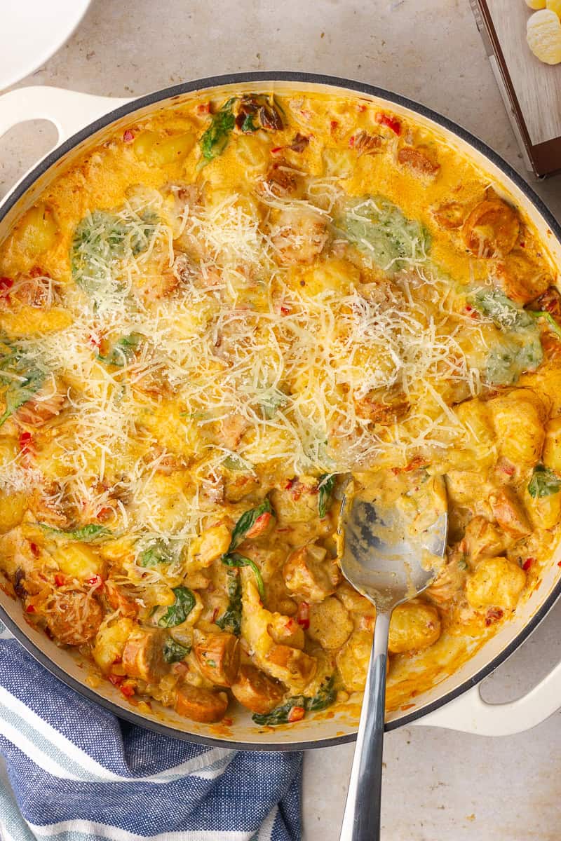 A spoon scoops into the finished cheesy Cajun gnocchi showing the creamy sauce and wilted spinach.