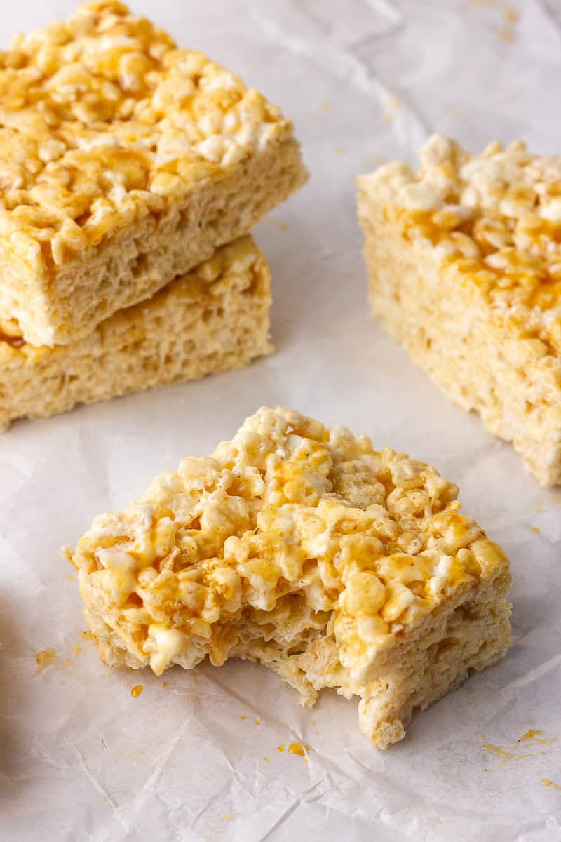 Cut caramel apple rice krispie treats sit on parchment with one treat showing a bite.