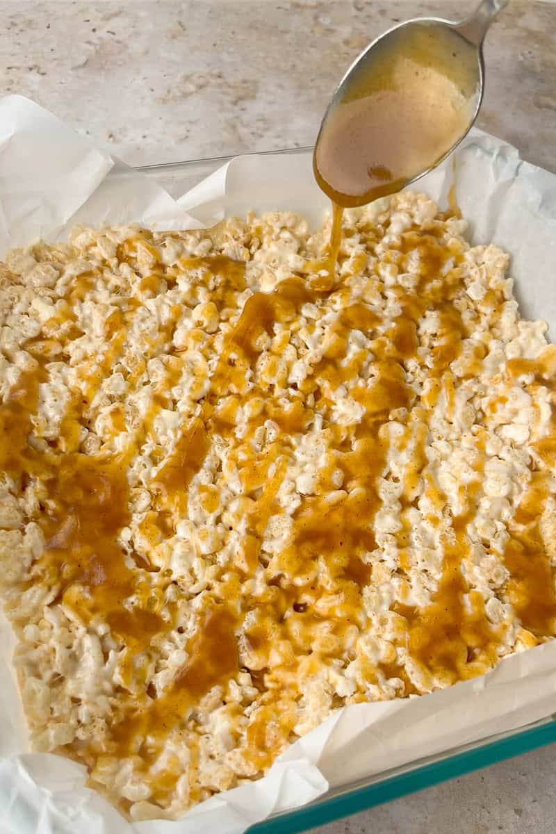 Warm caramel sauce is drizzled over the pressed Rice Krispie layer in the pan.
