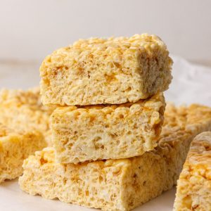 Three caramel apple Rice Krispie treats are stacked with more bars in the background.