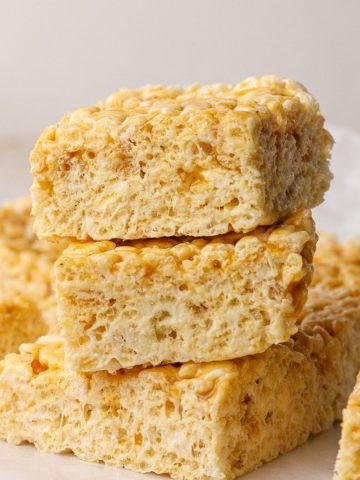 Three caramel apple Rice Krispie treats are stacked with more bars in the background.