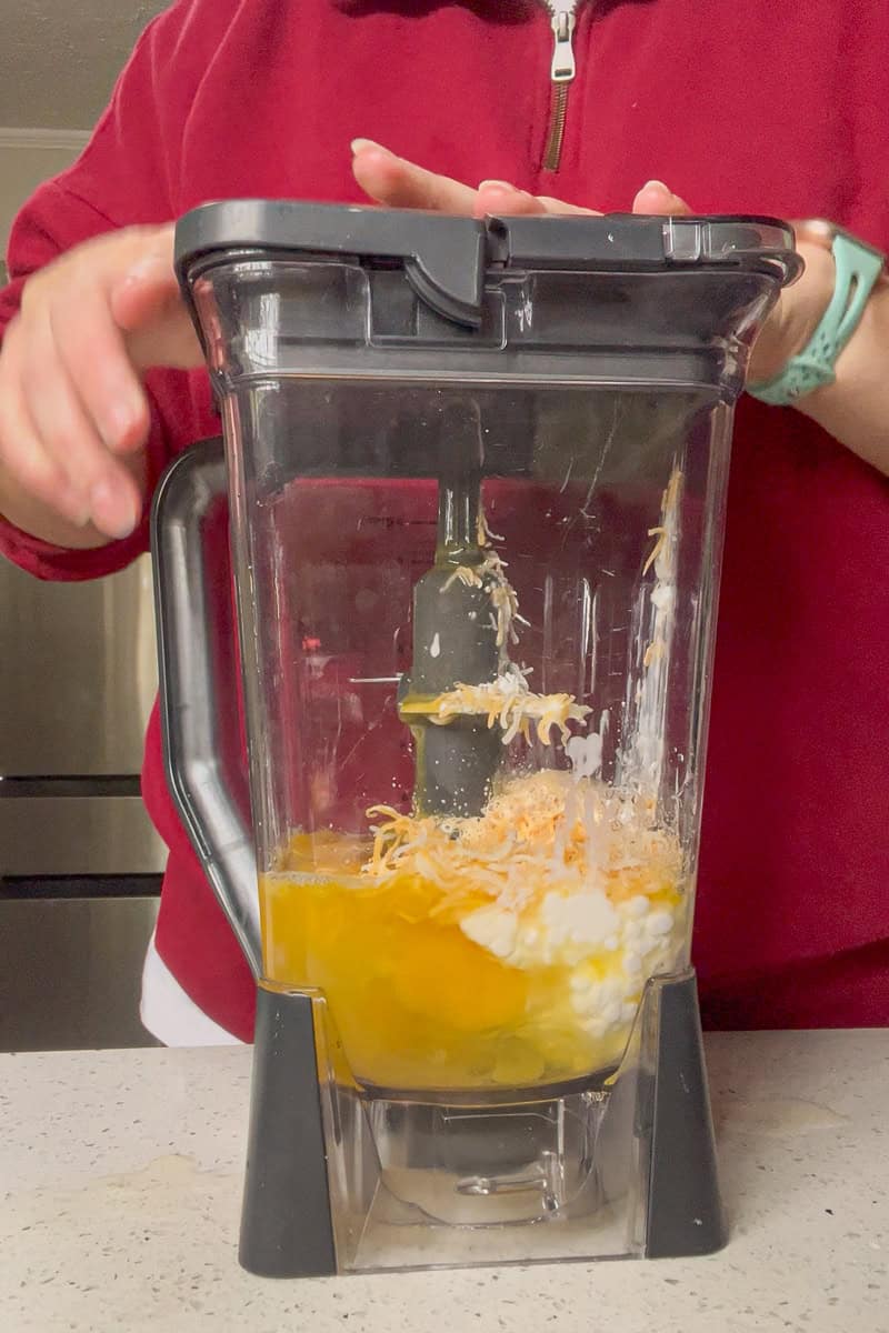 A blender filled with eggs, cottage cheese, and shredded cheese being blended for egg bites.