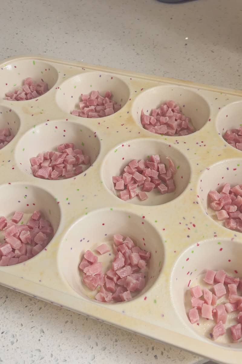 A muffin tin filled with diced ham pieces before adding the egg mixture.