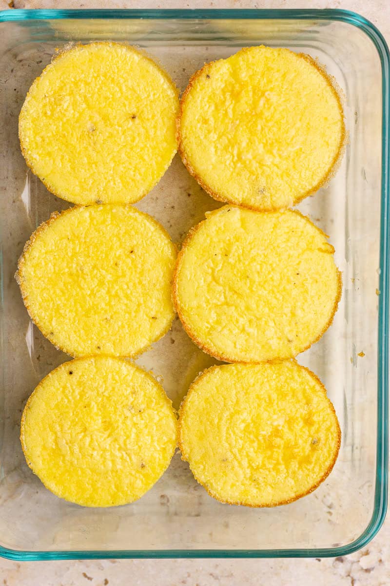 Six baked ham and cheese egg bites stored neatly in a glass meal prep container.