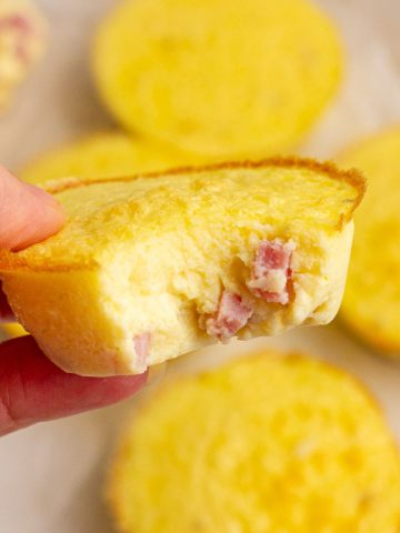 A hand holding a fluffy ham and cheese egg bite with more bites on parchment in the background.