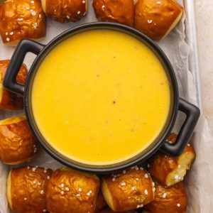 Finished pretzel cheese dip in a black bowl, surrounded by soft pretzel bites sprinkled with salt.