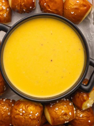 Finished pretzel cheese dip in a black bowl, surrounded by soft pretzel bites sprinkled with salt.
