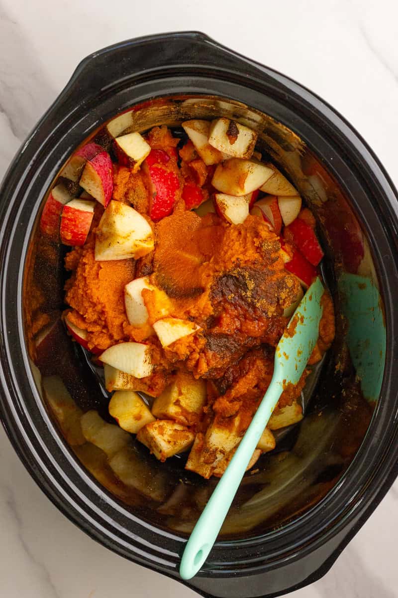 Ingredients for pumpkin apple butter, including chopped apples, pumpkin puree, and spices inside a slow cooker before cooking.