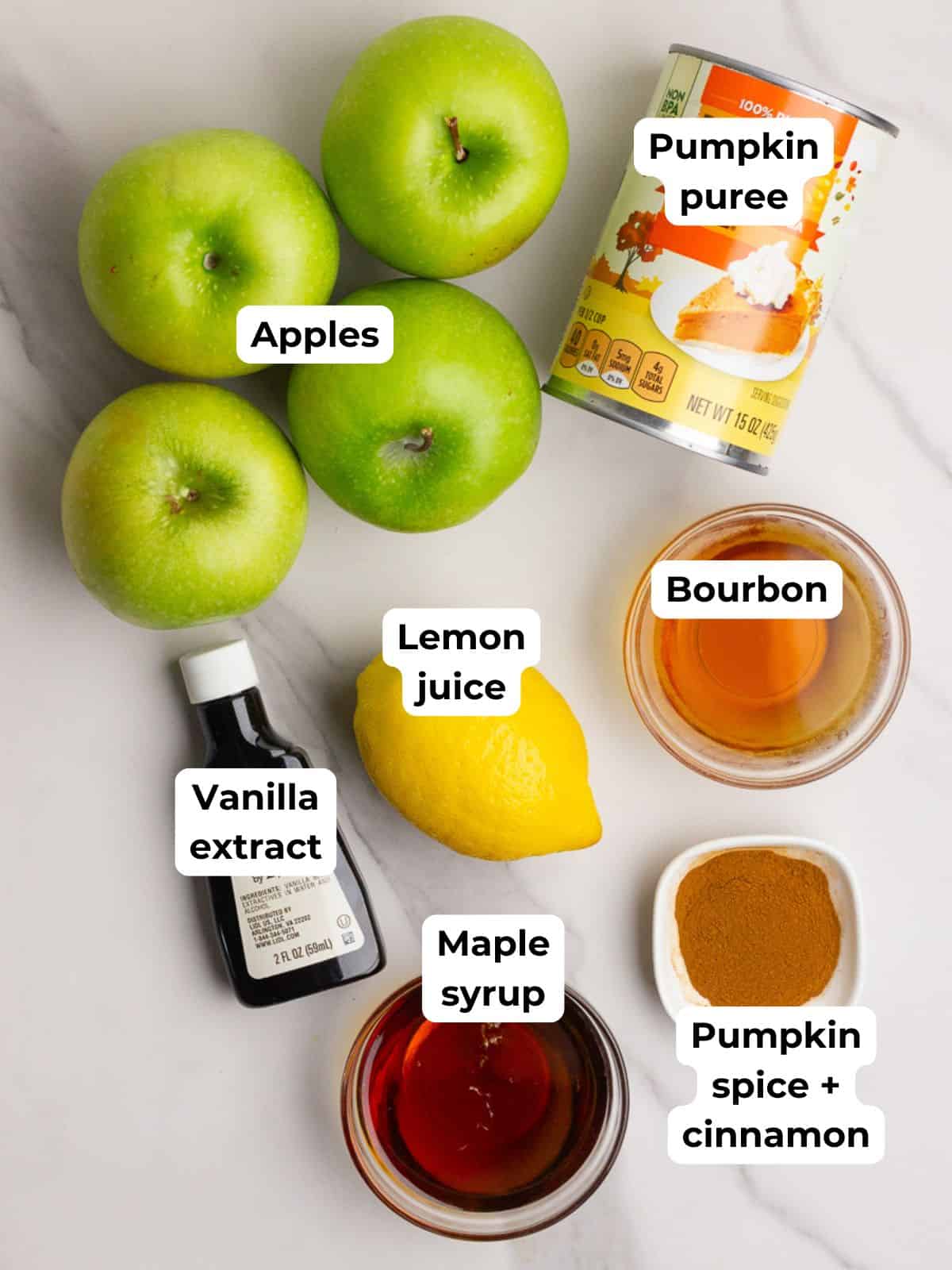 Overhead view of pumpkin apple butter ingredients including apples, pumpkin puree, lemon, bourbon, maple syrup, and spices.