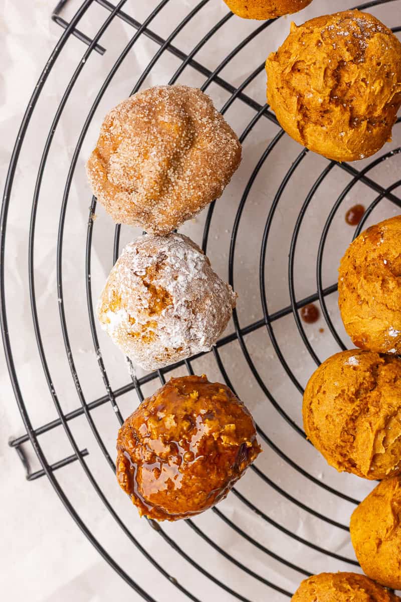Three donut holes on a rack showing cinnamon sugar, powdered sugar, and maple glaze coatings.