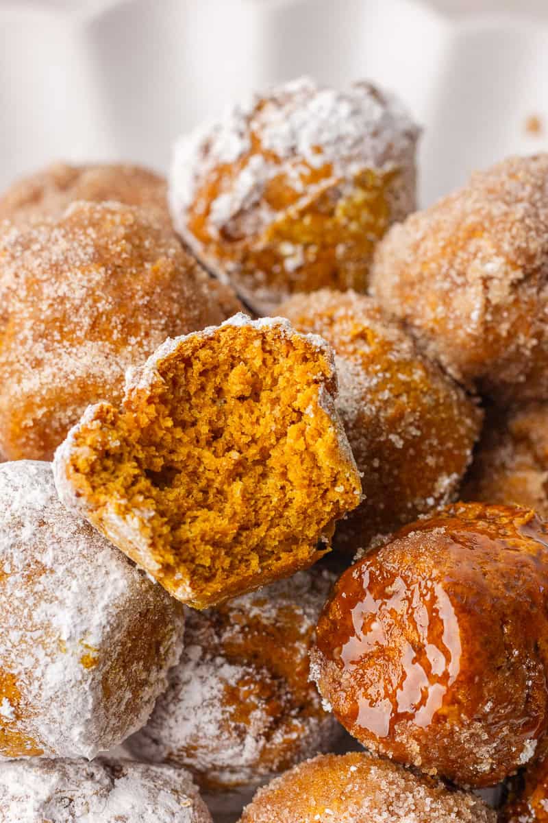 Close-up of a pile of pumpkin donut holes with one broken open to show the soft center.