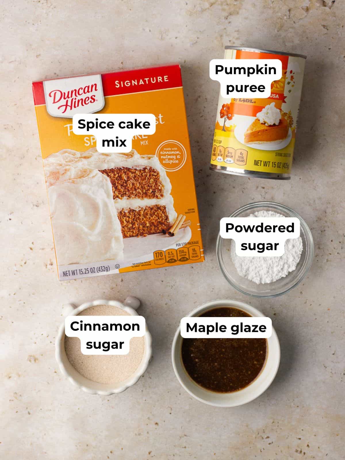 Flat lay of spice cake mix, pumpkin purée, and bowls of cinnamon sugar, powdered sugar, and maple glaze.