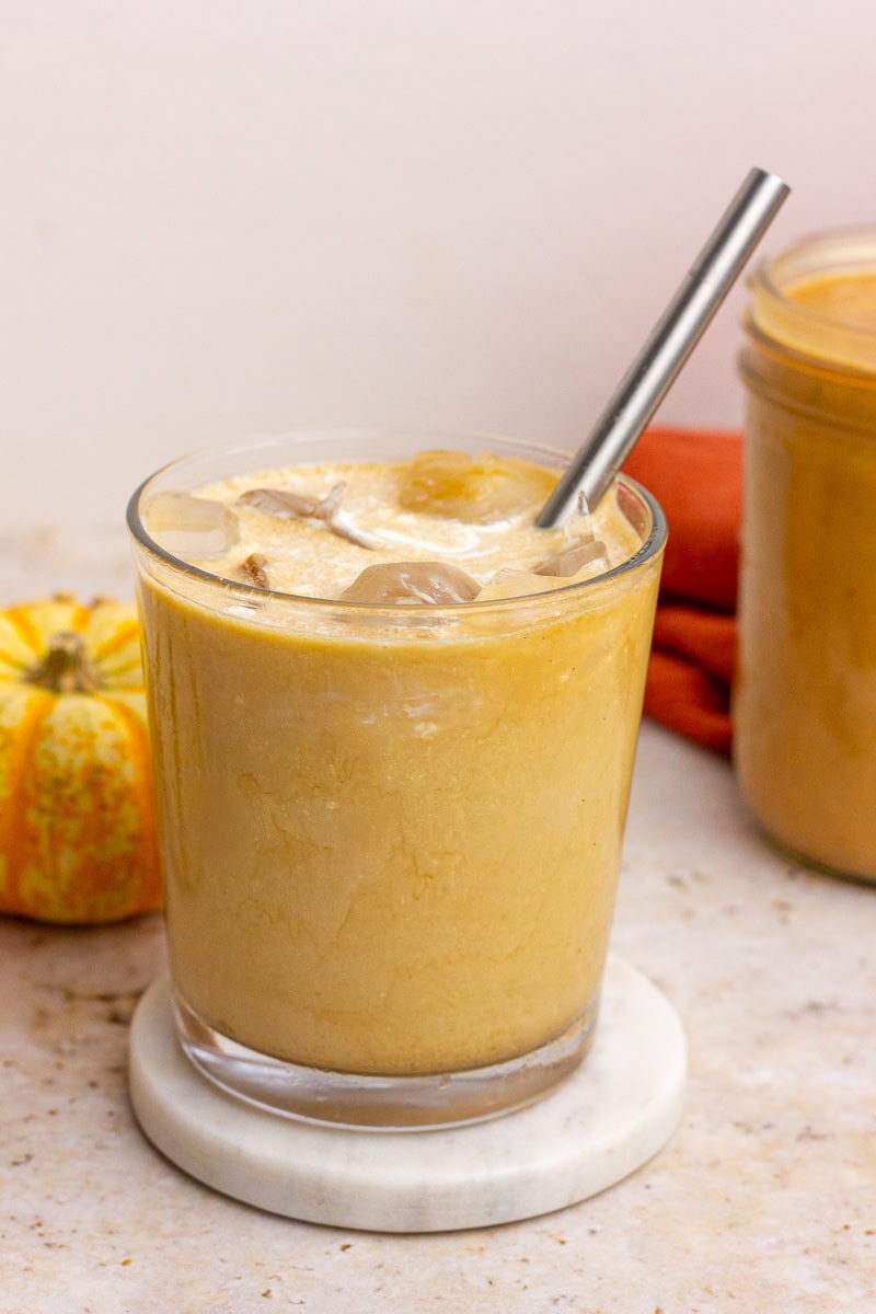 A glass of iced pumpkin spice latte made with homemade pumpkin spice sauce, shown with a metal straw and mini pumpkin in the background.