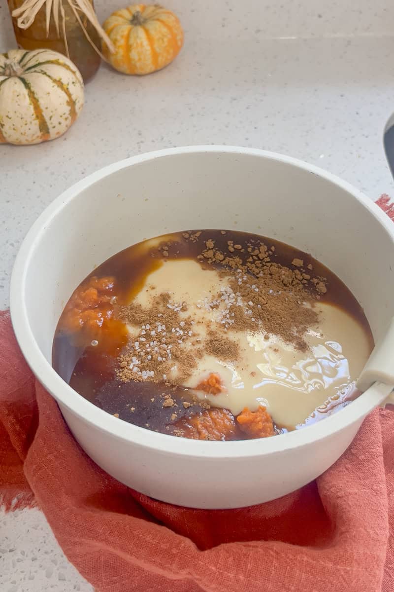 A saucepan filled with pumpkin puree, sweetened condensed milk, brown sugar, and spices ready to be whisked together.