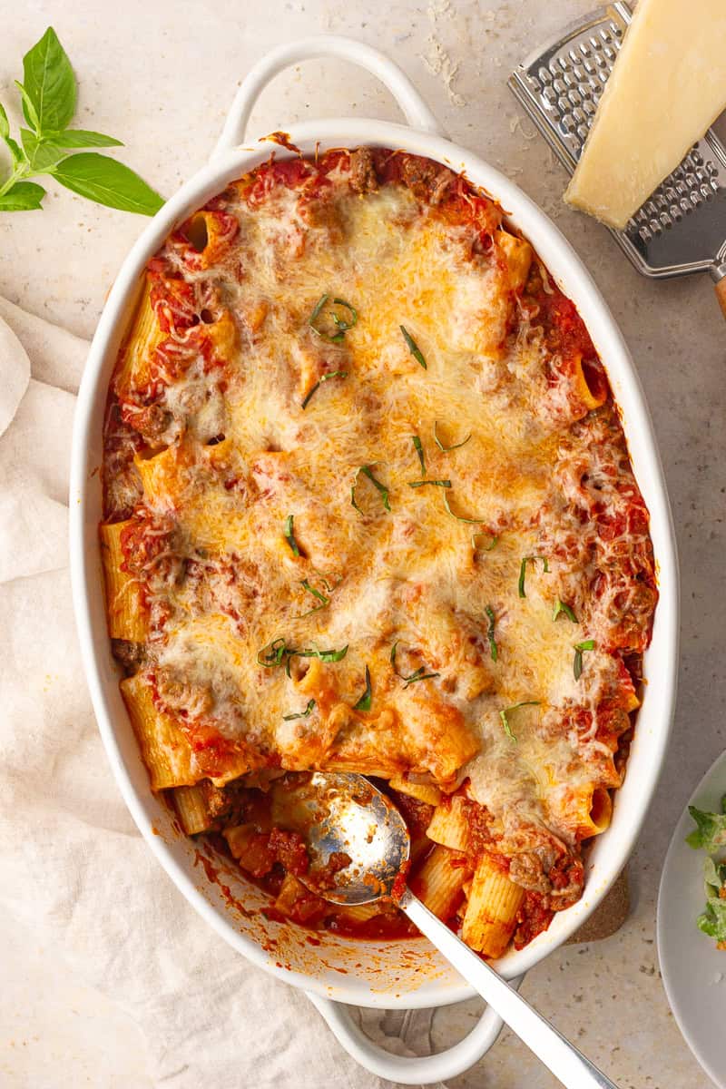 A bubbly pan of rigatoni al forno with a spoonful missing, exposing tender pasta and meat sauce.
