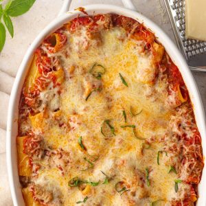 Overhead view of the finished rigatoni al forno with golden cheese and basil in a white baking dish.