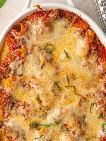 Overhead view of the finished rigatoni al forno with golden cheese and basil in a white baking dish.