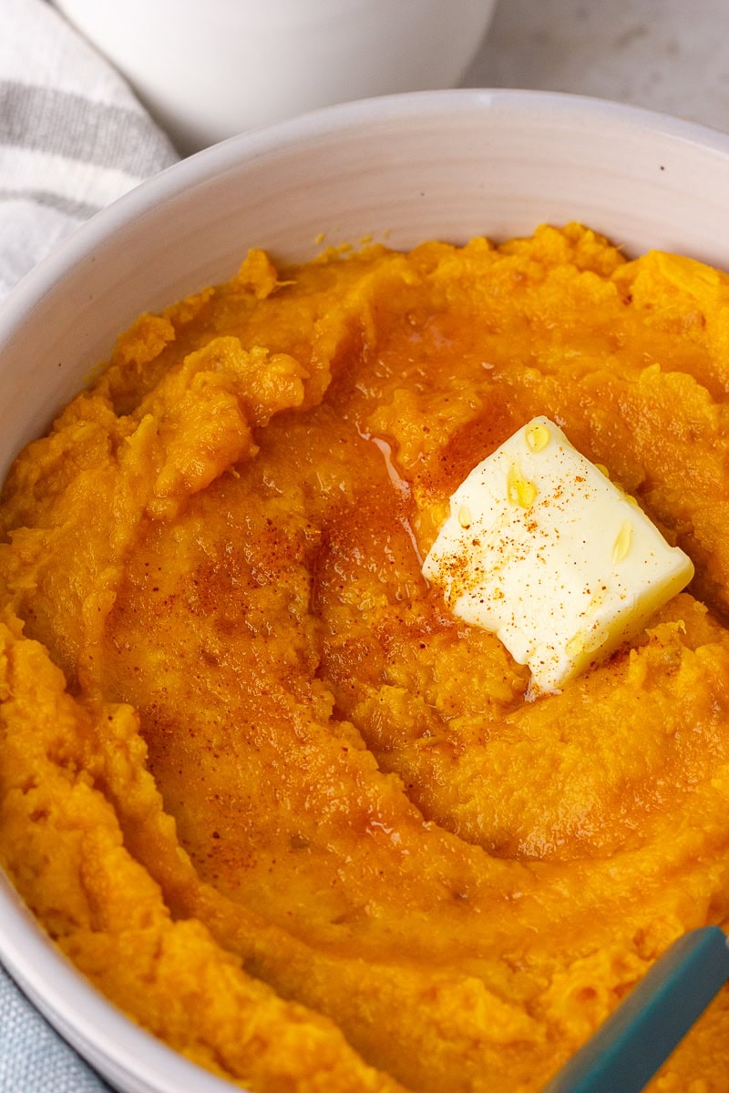Bowl of mashed sweet potatoes with melted butter and a swirl of hot honey on top.