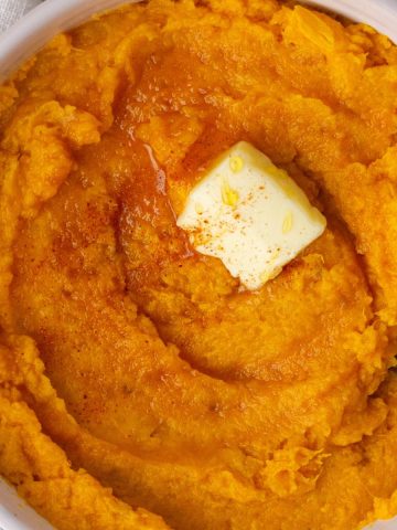 Close-up of spicy mashed sweet potatoes with melted butter and a sprinkle of paprika.