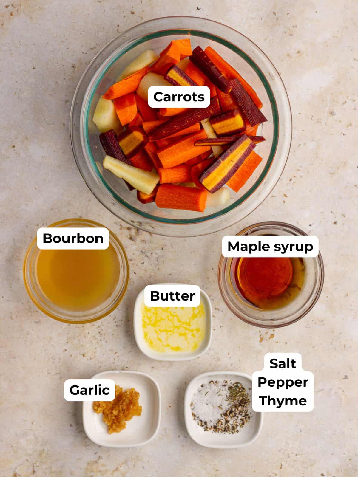 Ingredients for maple bourbon glazed carrots, including chopped carrots, melted butter, maple syrup, garlic, seasoning, and olive oil, are arranged on a countertop.