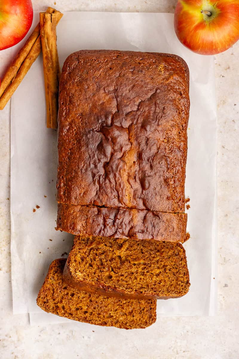 Overhead view of a loaf of apple butter bread with fresh apples and cinnamon sticks beside it.