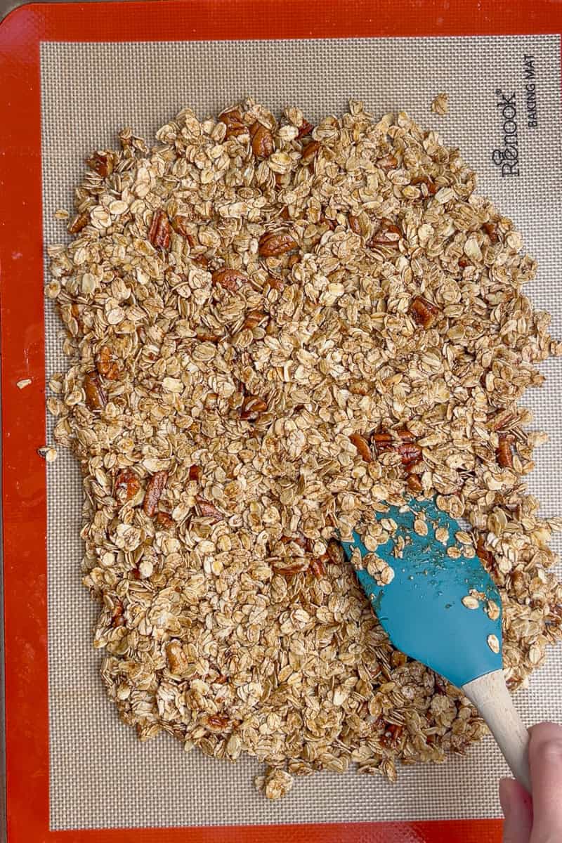 Granola mixture spread evenly on a silicone baking mat before baking.