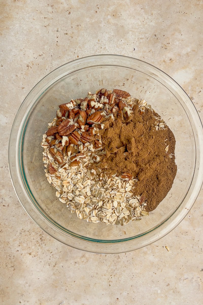 Mixing bowl filled with oats, pecans, and apple pie spice ready to make granola.