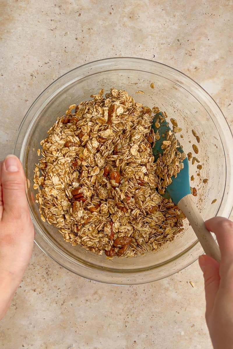Granola mixture being stirred with a spatula in a glass bowl before baking.