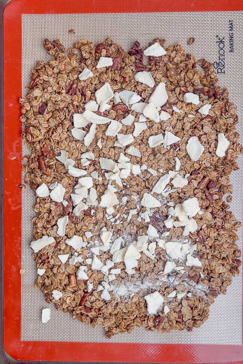 Baked granola cooling on a silicone mat topped with chopped freeze-dried apples.