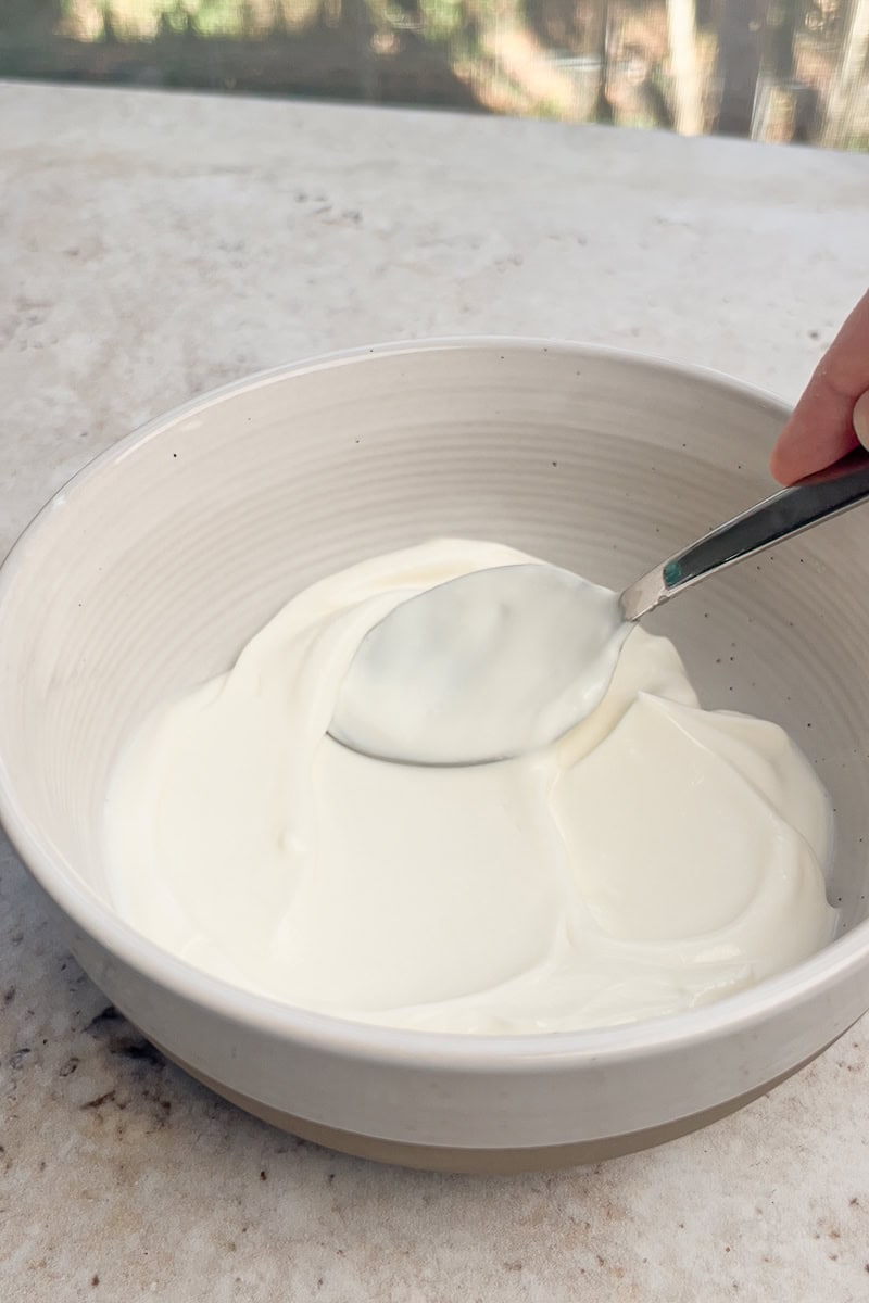 Bowl of smooth vanilla yogurt being spread with a spoon as the base for the recipe.