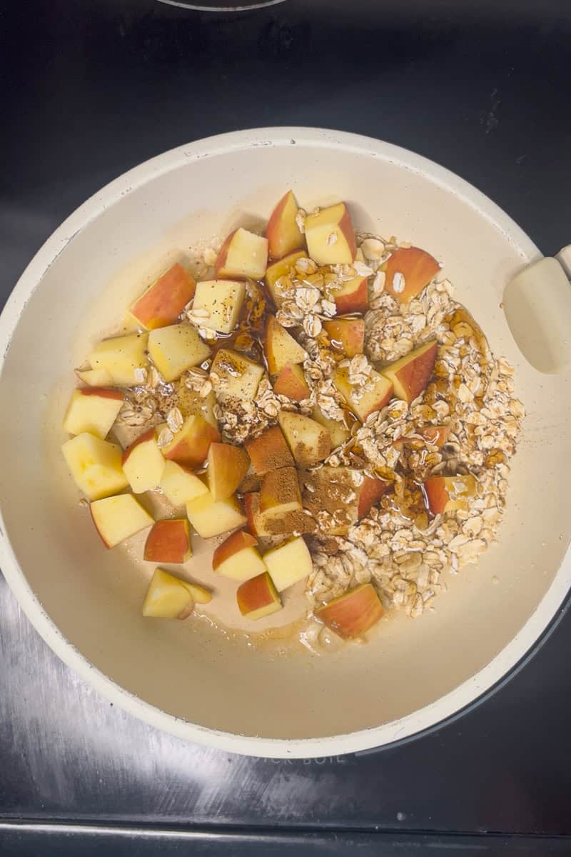Apples, oats, cinnamon, and maple syrup cooking together in a skillet for the topping.
