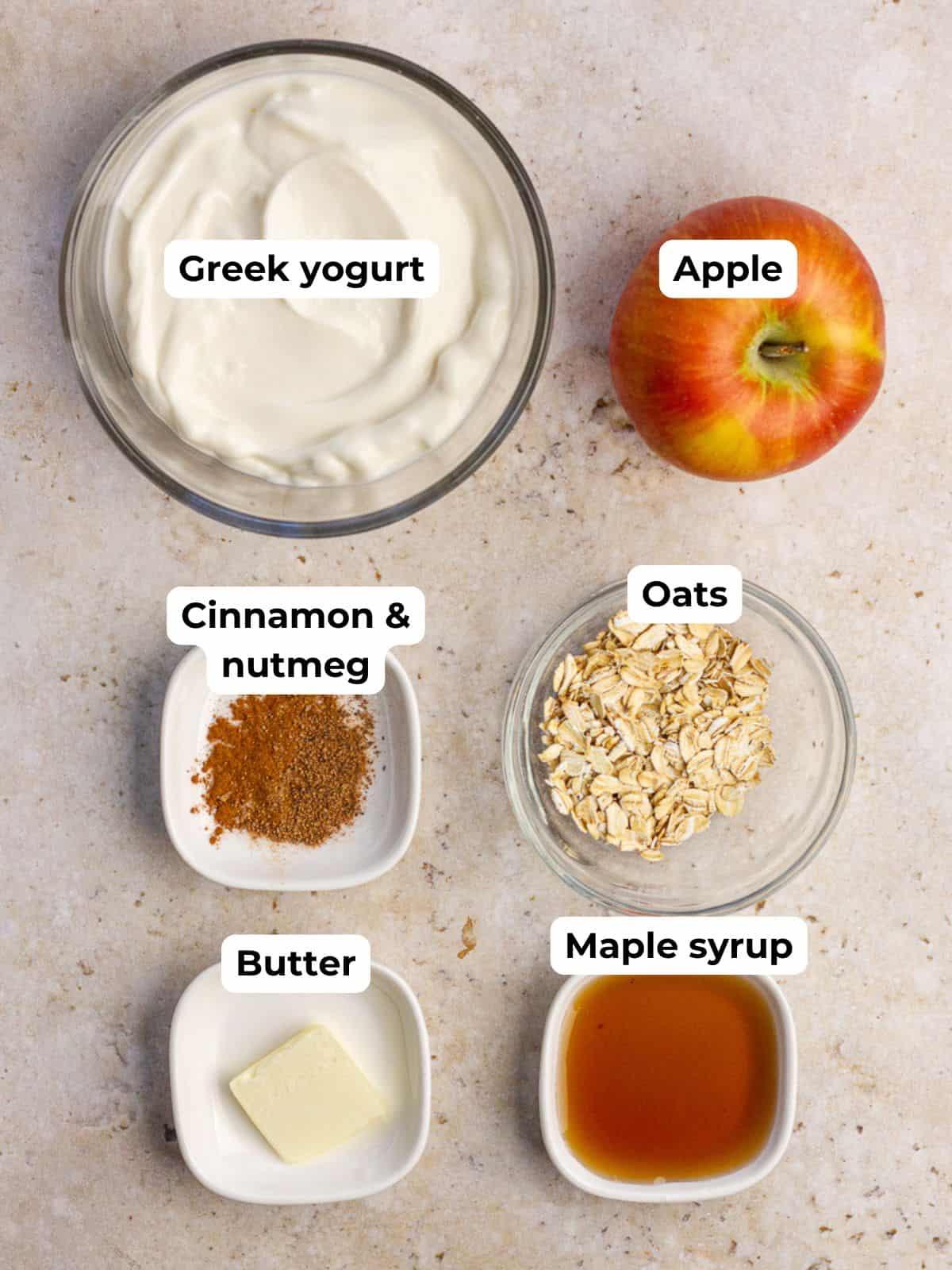 Ingredients laid out for the recipe including Greek yogurt, apple, oats, butter, maple syrup, cinnamon, and nutmeg.