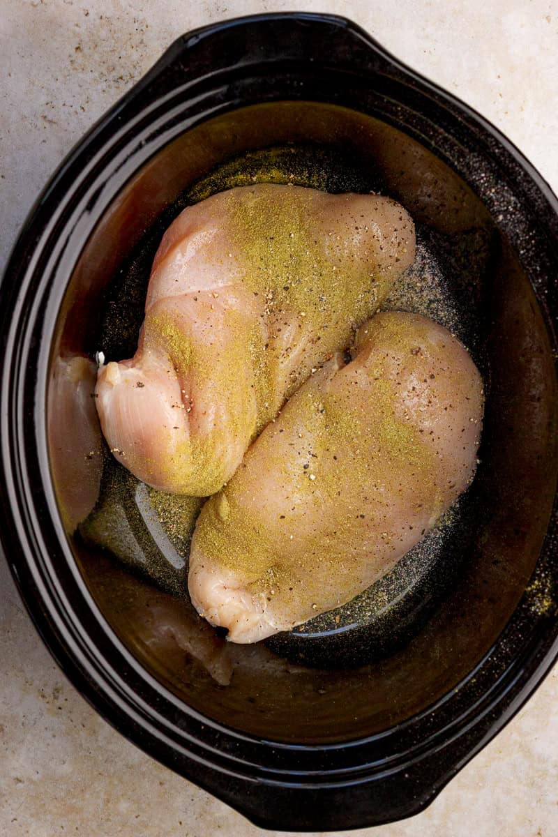 Seasoned chicken breasts sit in the bottom of a slow cooker.