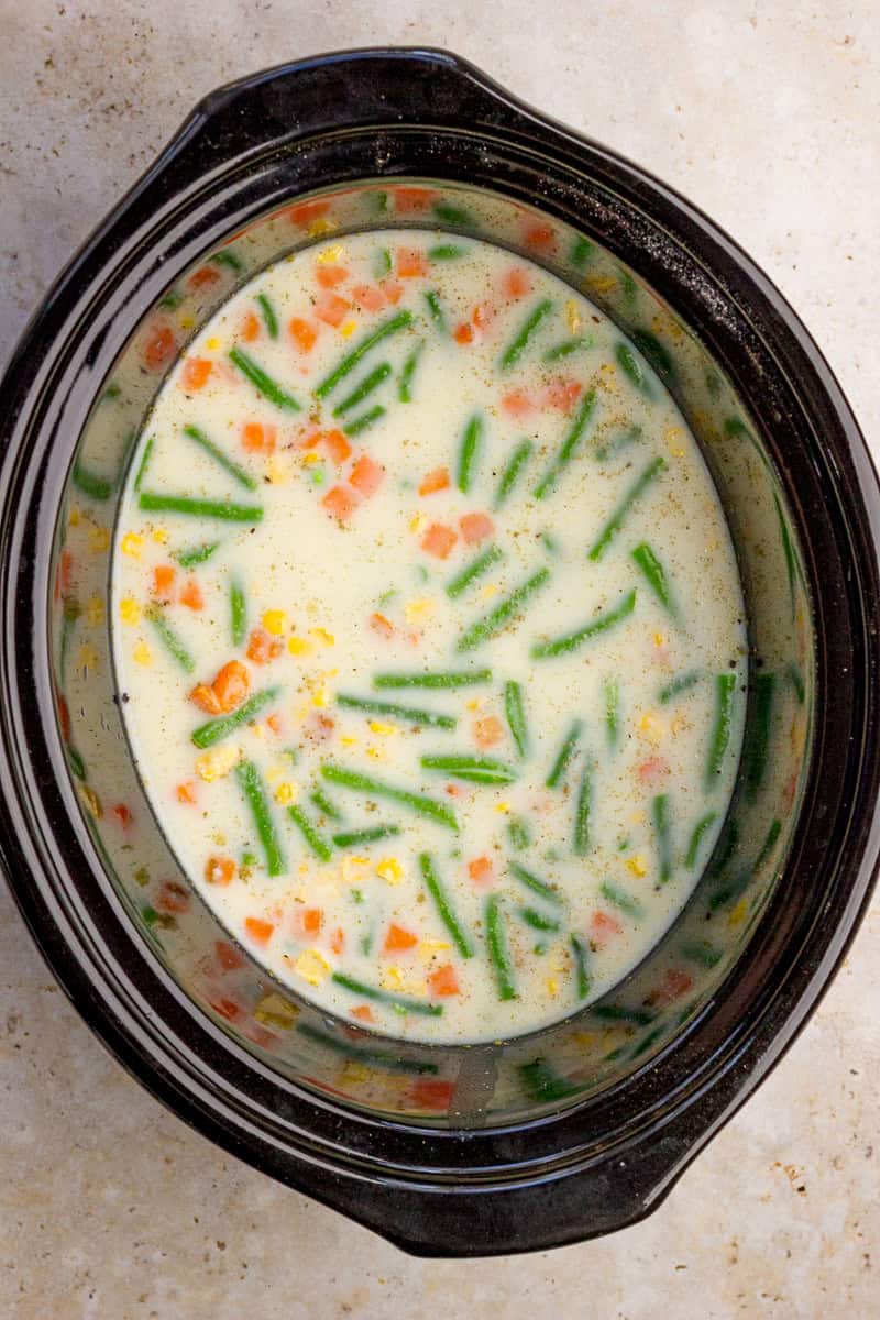 The slow cooker is filled with chicken, vegetables, and creamy broth before cooking.