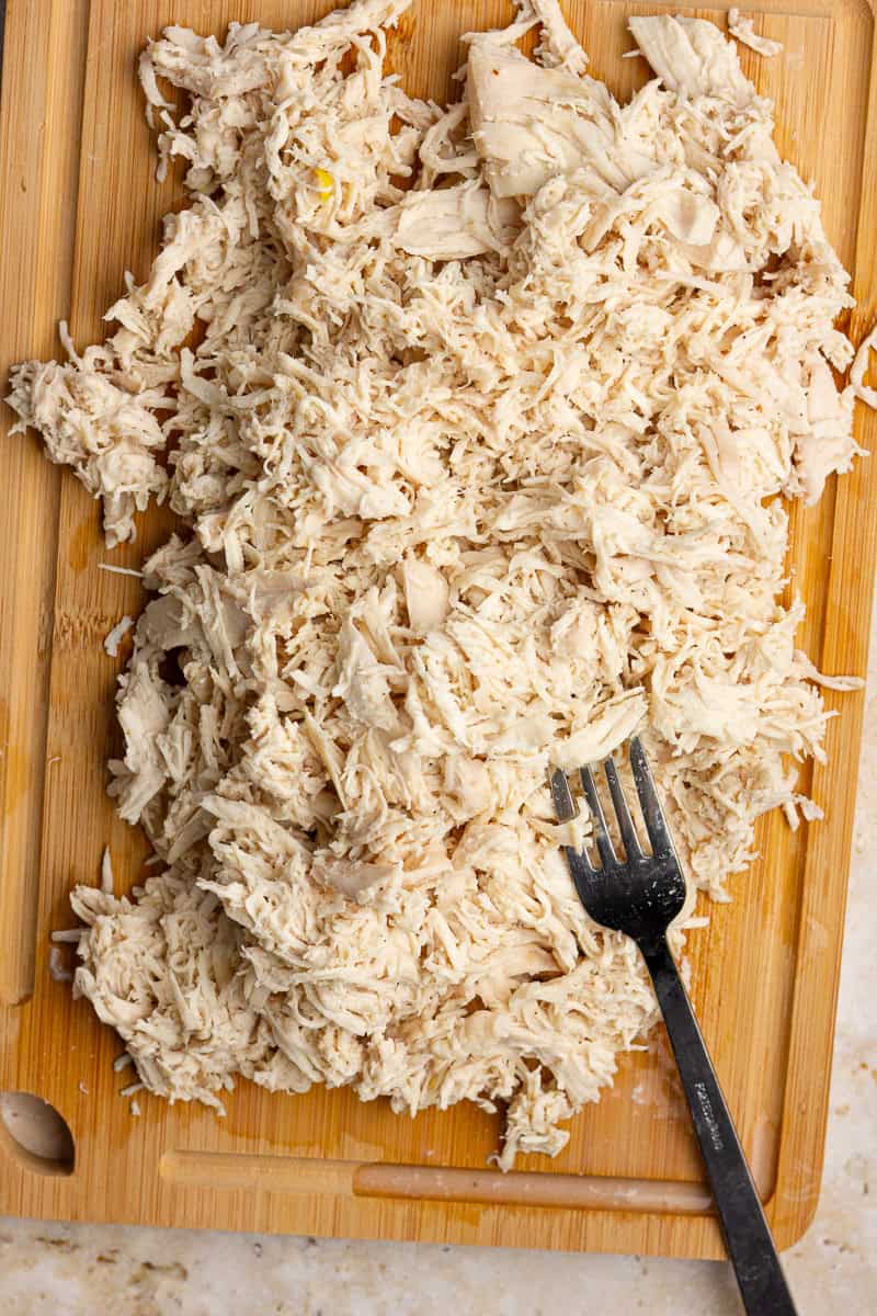 Shredded cooked chicken rests on a wooden cutting board with a fork.