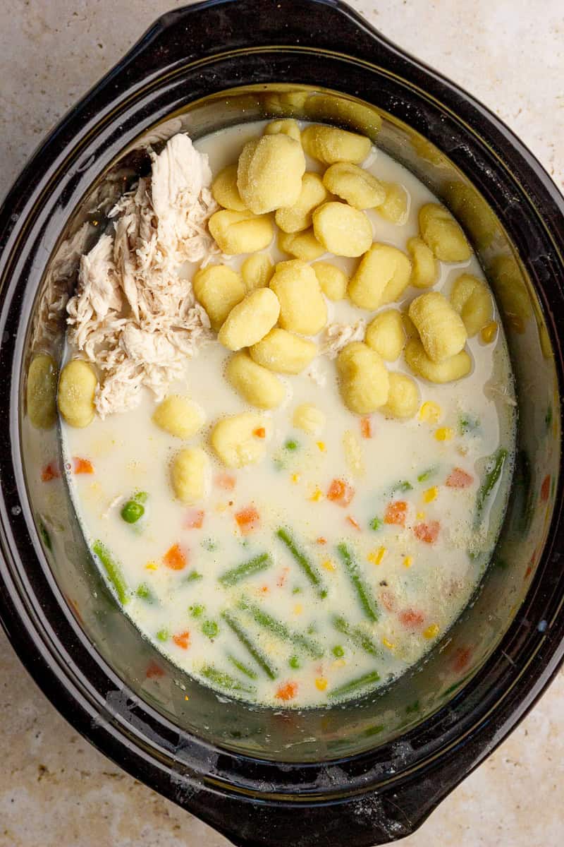 Shredded chicken and uncooked gnocchi sit in the creamy soup inside the slow cooker.