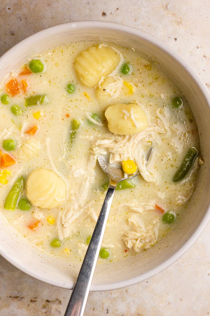 A bowl of chicken pot pie gnocchi soup shows tender chicken, vegetables, and soft gnocchi.