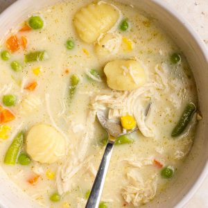 A close-up bowl of creamy chicken pot pie gnocchi soup with vegetables and gnocchi.