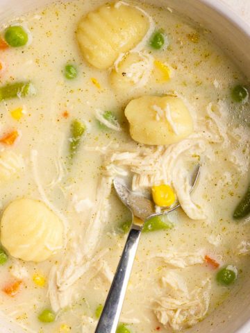A close-up bowl of creamy chicken pot pie gnocchi soup with vegetables and gnocchi.
