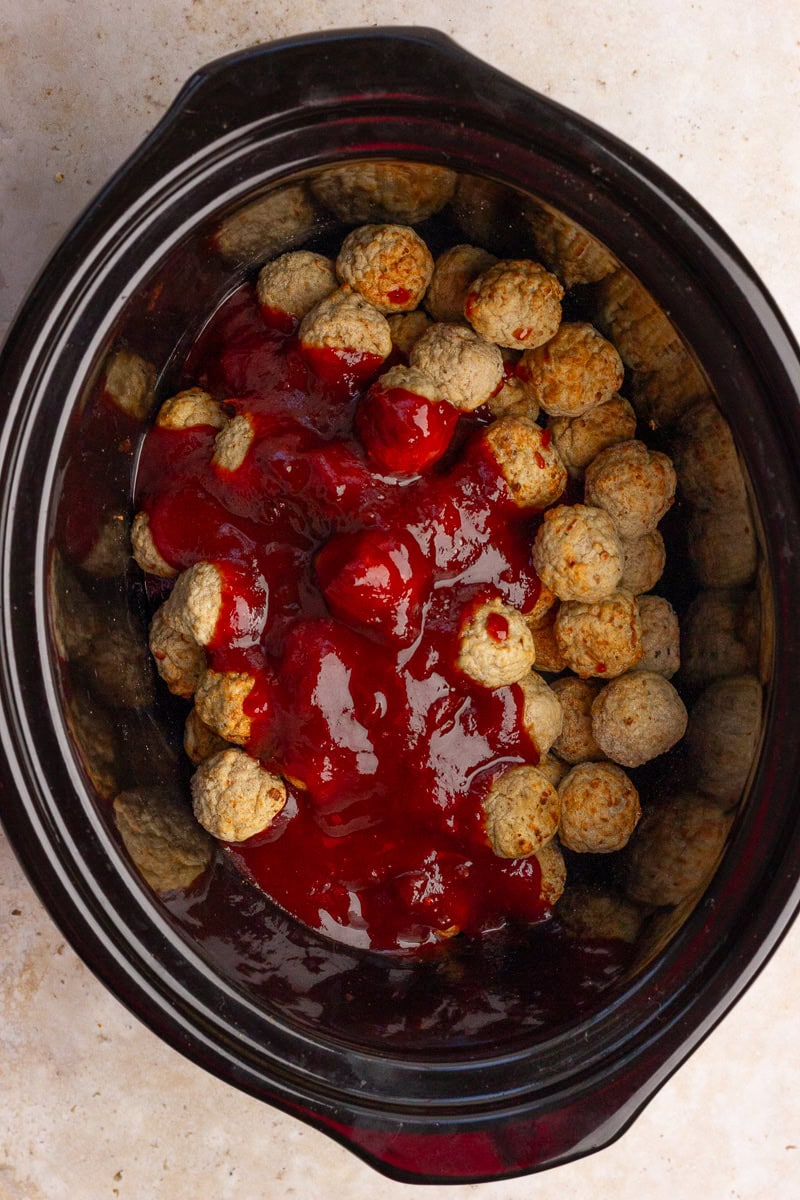 A slow cooker filled with frozen meatballs covered in warm cranberry barbecue sauce.