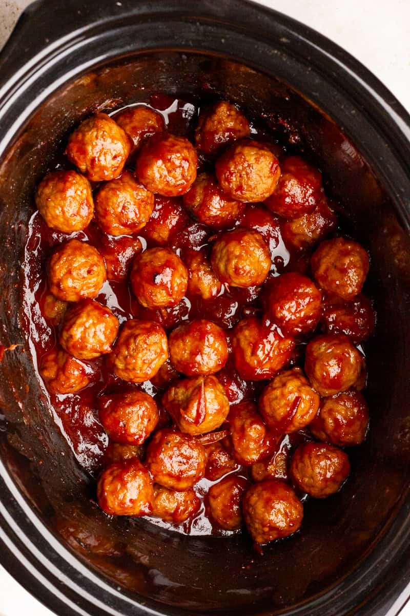 Cooked meatballs coated in a glossy cranberry barbecue sauce inside a slow cooker.